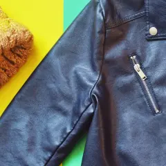 Veste en simili cuir noire et bonnet jaune sur fond coloré. Apprenez comment nettoyer une veste en simili cuir pour qu'elle reste comme neuve.