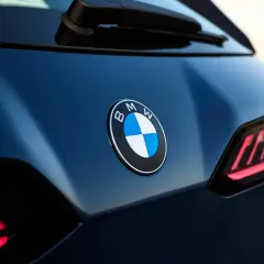 Nowe znaczki samochodowe BMW błyszczą na ciemnoniebieskim lakierze. Widoczne są charakterystyczne tylne światła.