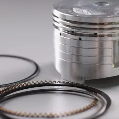 Partes de un pistón: un pistón metálico con ranuras y anillos de compresión y de aceite dispuestos a su lado.