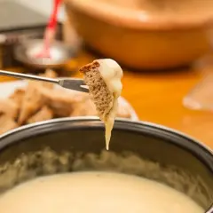 Un morceau de pain trempé dans une fondue savoyarde sans appareil. Le fromage dégouline sur la fourchette.