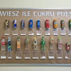 Tablica edukacyjna pokazuje, ile cukru jest w popularnych napojach. Obok każdej butelki i puszki znajduje się woreczek z odpowiadającą ilością kostek cukru.
