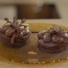 Dos bizcochos sin harina de chocolate, decorados con crema y avellanas, sobre un plato dorado.