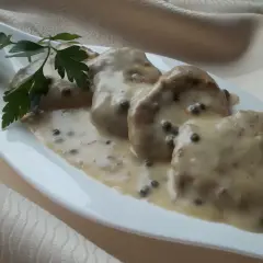 Polędwiczki w sosie z zielonego pieprzu, udekorowane natką pietruszki, prezentują się apetycznie na białej, łódkowatej zastawie.