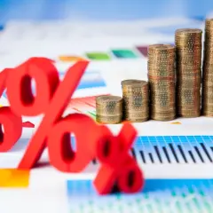 Rote Prozentzeichen und Münzstapel auf Finanzdiagrammen. Sie fragen sich, was sind Zinsen? Hier sehen Sie die Antwort visuell dargestellt.