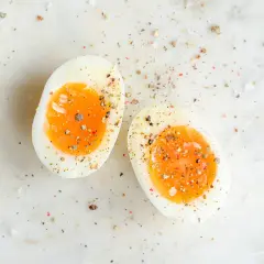 Deux moitiés d'oeuf dur trop cuit, saupoudrées de sel et de poivre, sur une surface marbrée.
