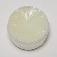 Un recipiente abierto con petrolatum, una sustancia blanca y translúcida, con marcas radiales en su superficie.