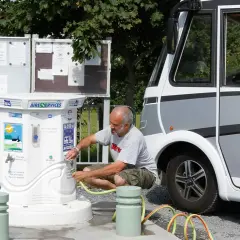 Un homme remplit un tuyau à un point d'eau pour camping-car. L'aire de services propose de l'eau potable et non potable.