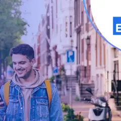Uśmiechnięty mężczyzna z telefonem w ręku, w tle ulica z budynkami i skuterem. Promocja Santander lokata 3-miesięczna.