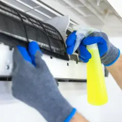 Manos enguantadas sacan filtro de aire acondicionado para limpiarlo con spray.