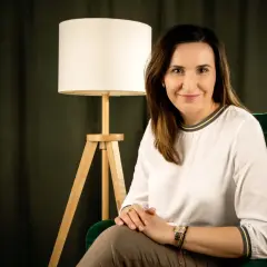 Kobieta w białej bluzce siedzi w zielonym fotelu obok lampy.