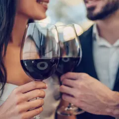 Ein Paar hebt Gläser mit Rotwein zum Anstoßen. Ein Glas Rotwein kann gesund sein, wenn er in Maßen genossen wird.