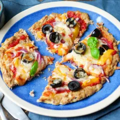 Low carb pizza thunfisch mit Oliven und Paprika auf blauem Teller, daneben eine Schale mit Tomatensauce und frischem Basilikum.