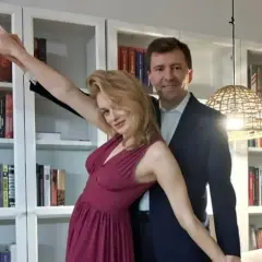 Łukasz Schreiber z żoną pozują na tle regałów z książkami. Ona w błyszczącej sukni, on w garniturze.