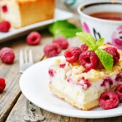 Ania gotuje malinowa chmurka. Pyszny sernik z malinami i kruszonką, ozdobiony świeżymi malinami i miętą, czeka na filiżankę herbaty.
