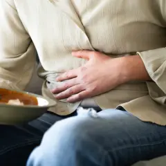 Osoba trzymająca miskę z jedzeniem, masująca brzuch z powodu wzdęć po jedzeniu.