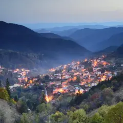Wieczorna panorama gór w Bułgarii. W dolinie rozświetlona wioska, otoczona lasami i łagodnymi wzgórzami.