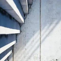 Ombre et lumière sur un mur en béton cellulaire, révélant des traces d'humidité et de légères fissures.