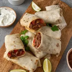 En hög med saftiga chicken burritos på en träskärbräda, serverade med gräddfil, salsa och limeklyftor.