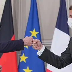 Olaf Scholz und Emmanuel Macron stoßen Fäuste vor den Flaggen von Deutschland und Frankreich.