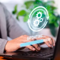 Osoba w garniturze pracuje na laptopie, na ekranie widoczny pasek postępu "UPDATING..." i ikona aktualizacji. Dowiedz się, jak zaktualizować Windows 10.