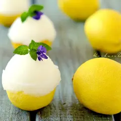 Orzeźwiający sorbet cytrynowy podany w wydrążonych cytrynach, udekorowany miętą i fioletowym kwiatkiem.