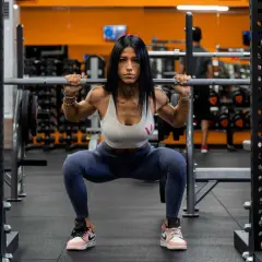 Donna determinata esegue squat con bilanciere in palestra. Gli squat fanno dimagrire e scolpiscono il corpo, un passo alla volta.