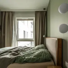 Przytulna sypialnia inspiracje: łóżko z zieloną pościelą, zasłony, okno i lampy ścienne tworzą relaksującą atmosferę.