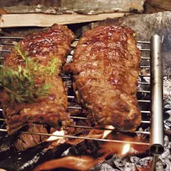 Två saftiga spareribs grillas över öppen eld. En hand lägger på en kvist rosmarin för extra smak.