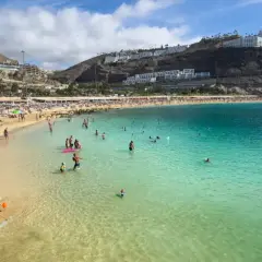 En livlig strand på Gran Canaria med solbadare, badande och en uppblåsbar vattenpark. En perfekt dag för att njuta av solen och havet.