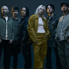 Sześcioro muzyków, w tym wokalistka w żółtym komplecie, pozuje do zdjęcia. Ich styl nawiązuje do **nu metal**owych klimatów.