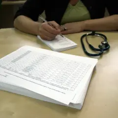 Stetoskop i dokumenty na biurku. Osoba pisze notatki, być może dotyczące ubezpieczenia zdrowotnego ZUS dla niepracujących.