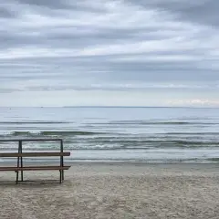 Pusta ławka na plaży w Gąskach, wpatrzona w spokojne morze pod zachmurzonym niebem.