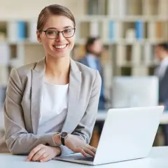 Lächelnde Frau mit Brille am Laptop, bereit für ihre medizinische Schreibkraft Ausbildung.