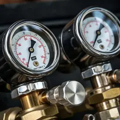 Dwa manometry wskazujące ciśnienie gazu, połączone z mosiężnymi elementami. Precyzyjny regulator ciśnienia gazu.
