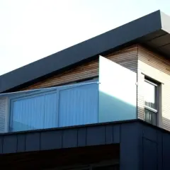 Nowoczesny budynek z drewnianą elewacją i szklanymi balustradami. Widać fragment dachu, który sugeruje, jak zrobić spadek na dachu płaskim.