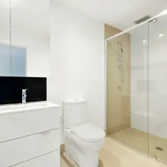 Mampara de ducha de cristal con medidas adecuadas para que no salga el agua. Baño moderno con lavabo, inodoro y ducha.