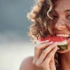 En glad kvinna med lockigt hår njuter av en saftig vattenmelon. Kanske en gravid kvinna som får sitt sug!