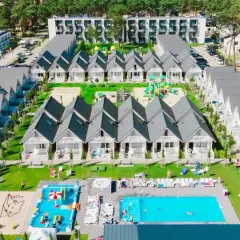 Widok z lotu ptaka na holiday park Kołobrzeg: rzędy białych domków z szarymi dachami, baseny, plac zabaw i zielone tereny.