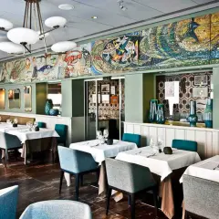 Interni eleganti di un ristorante, con tavoli apparecchiati e un grande mosaico marino sul muro. Un luogo ideale per scoprire i migliori ristoranti di pesce a Milano.