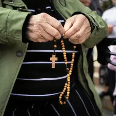 Dłoń starszej osoby trzyma paciorki różańca, odmawiając modlitwę do anioła stróża za dorosłe dzieci.