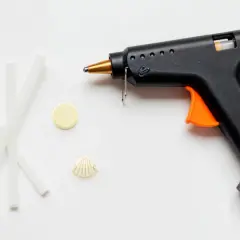Pistolet do kleju na gorąco, kilka pałeczek kleju, muszelka i żółty krążek. Czy klej na gorąco przewodzi prąd?