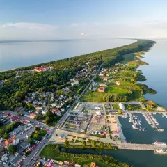 Widok z lotu ptaka na Krynicę Morską. Widać zalew, lasy, zabudowania i tętniący życiem rynek z mariną pełną łodzi.