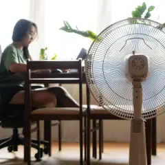 Kobieta pracuje przy biurku, a obok stoi wentylator pokojowy. Zastanawiasz się, ile prądu zużywa wentylator pokojowy?