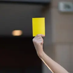 Ręka trzymająca żółtą kartkę, jak w piłce nożnej.