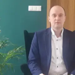Mężczyzna w garniturze siedzi w fotelu obok rośliny.