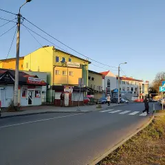 Ulica w Kleosinie z kolorowymi budynkami, sklepami i przejściem dla pieszych.