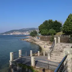 Vista de la playa de las barcas con gente disfrutando del sol y el mar. Al fondo, un puente y una ciudad en la ladera de una montaña.