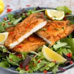 Knuspriges, low carb Putenschnitzel auf einem Salatbett mit Zitronenspalten und Paprikastückchen.