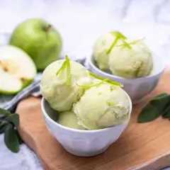 Orzeźwiający sorbet jabłkowy w miseczkach, udekorowany skórką z limonki. Obok całe i połówka zielonego jabłka.