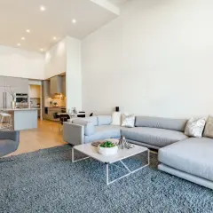 Nowoczesny salon z szarą sofą i fotelem, otwartą kuchnią i jadalnią. Idealne wnętrze do życia, jak w ofercie Vinci Immobilier Polska.